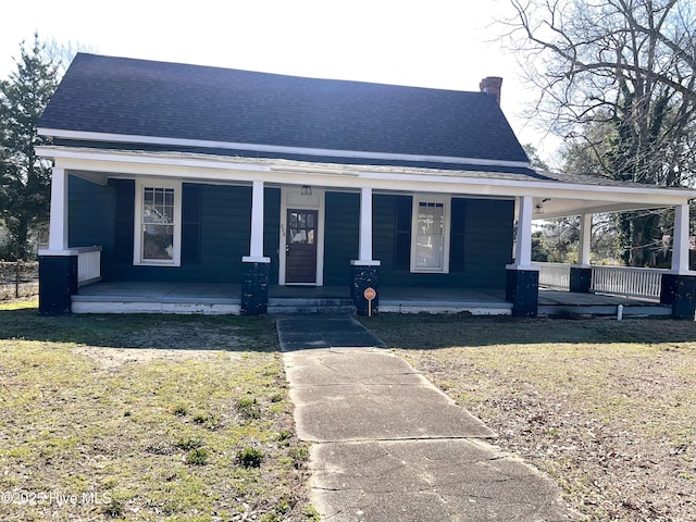 view of front of property with a front yard, covered porch, roof with shingles, and a chimney