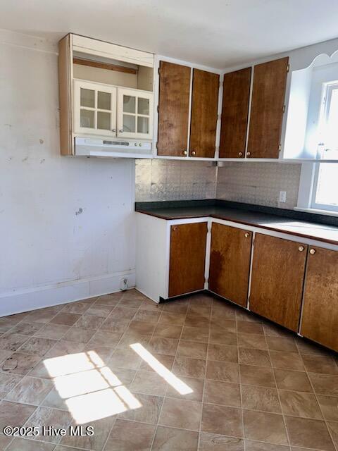 kitchen with baseboards, backsplash, brown cabinets, and range hood