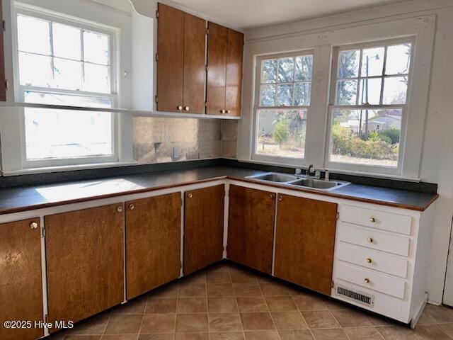 kitchen featuring a sink, brown cabinets, dark countertops, and a healthy amount of sunlight