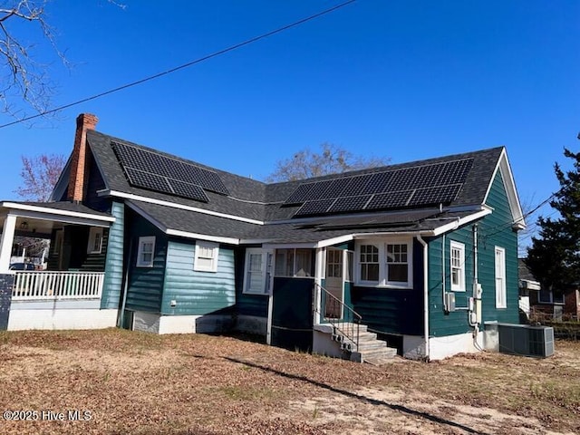 view of front facade with central air condition unit, solar panels, and roof with shingles