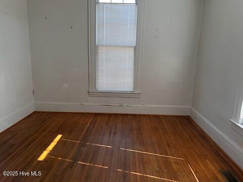 unfurnished room featuring visible vents, wood finished floors, and baseboards