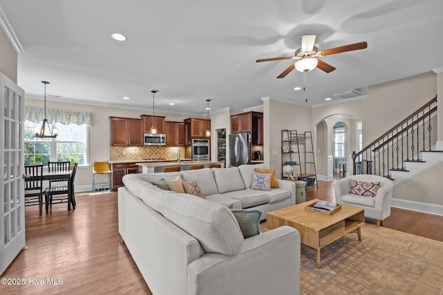 living room featuring a ceiling fan, baseboards, arched walkways, ornamental molding, and light wood-type flooring