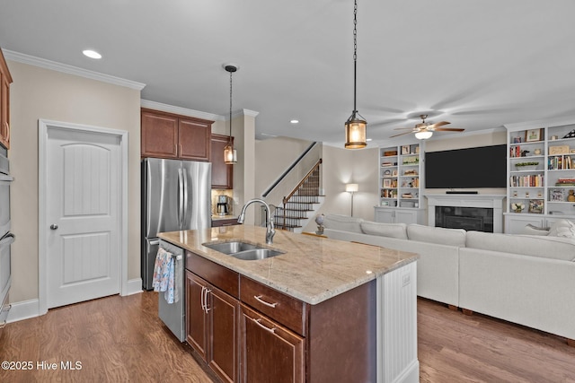 kitchen featuring a sink, a tile fireplace, stainless steel appliances, a ceiling fan, and dark wood-style flooring