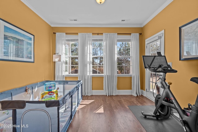 exercise area featuring baseboards, wood finished floors, visible vents, and ornamental molding