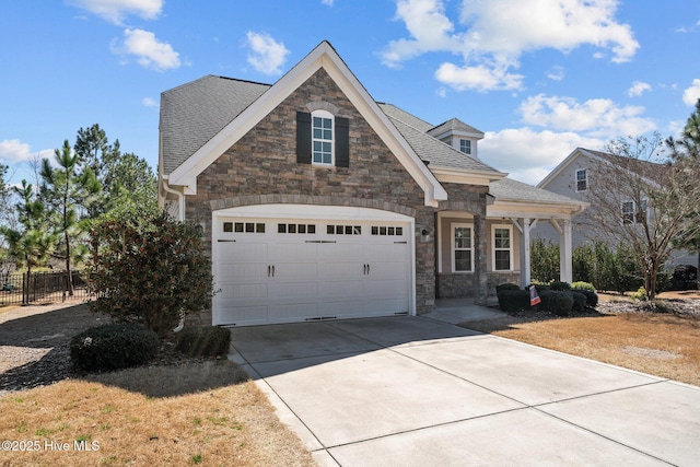 view of front facade featuring fence, a shingled roof, concrete driveway, a garage, and stone siding