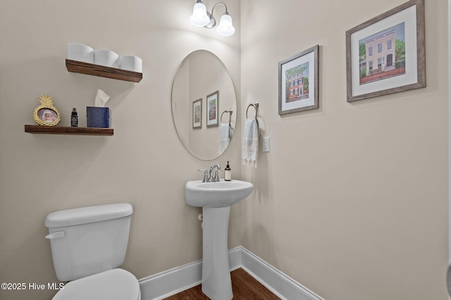 half bath with a sink, baseboards, toilet, and wood finished floors