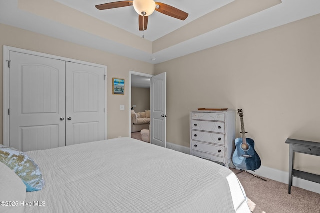 carpeted bedroom with a tray ceiling, baseboards, a closet, and a ceiling fan