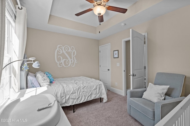 carpeted bedroom featuring ceiling fan, a raised ceiling, and baseboards