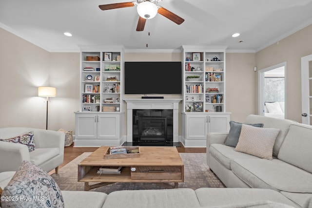 living room featuring wood finished floors, a ceiling fan, recessed lighting, a glass covered fireplace, and crown molding