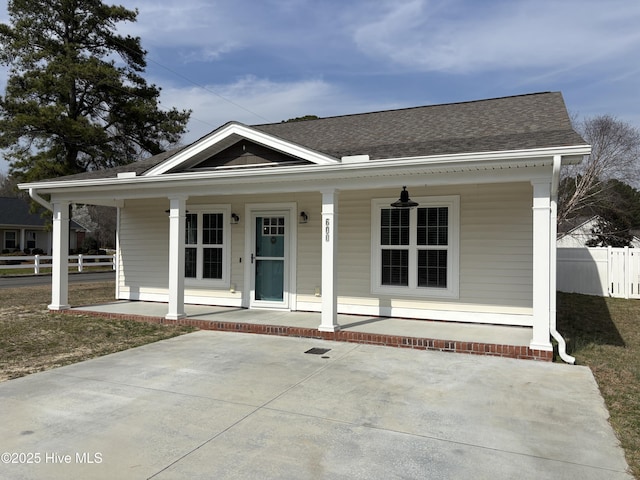 view of front facade featuring fence, covered porch, and roof with shingles