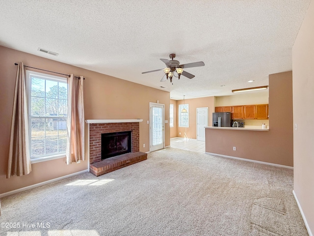 unfurnished living room with a ceiling fan, baseboards, visible vents, light carpet, and a brick fireplace