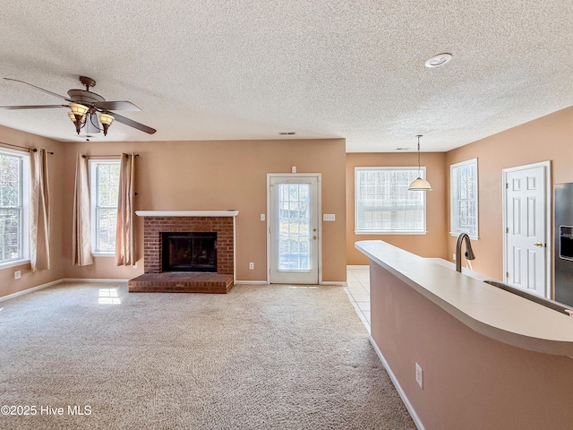 unfurnished living room featuring light colored carpet, a brick fireplace, a healthy amount of sunlight, and a sink