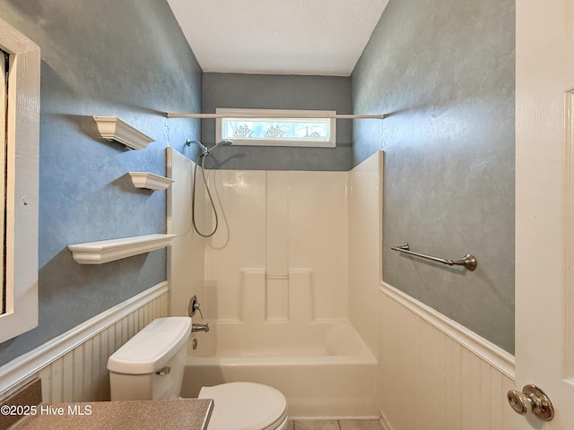 bathroom featuring a wainscoted wall, a textured ceiling, toilet, and shower / bathtub combination