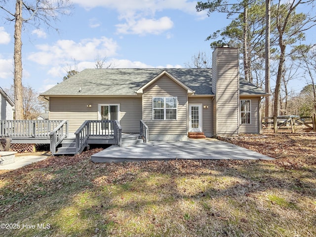 rear view of property with a shingled roof, a patio, a wooden deck, and a chimney