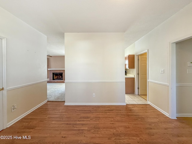 empty room with light wood-style flooring, a brick fireplace, and baseboards