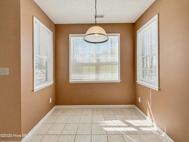 unfurnished dining area featuring light tile patterned floors, baseboards, visible vents, and a textured ceiling