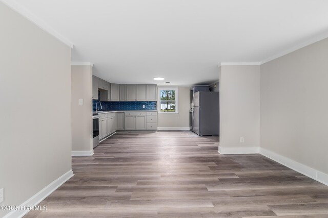 kitchen with tasteful backsplash, gray cabinetry, baseboards, freestanding refrigerator, and wood finished floors