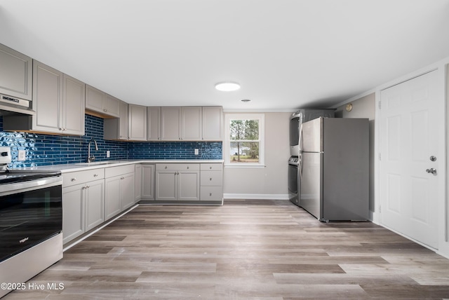 kitchen featuring backsplash, light wood-type flooring, light countertops, appliances with stainless steel finishes, and a sink