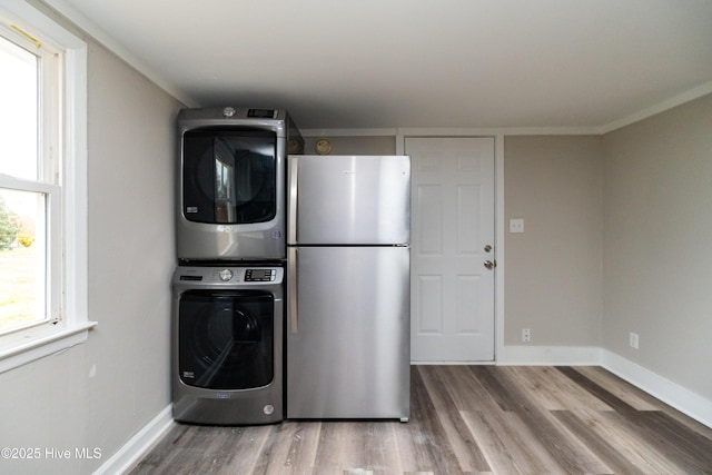 laundry room featuring baseboards, wood finished floors, and stacked washer / dryer