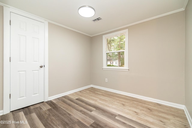 empty room with light wood-type flooring, visible vents, baseboards, and crown molding