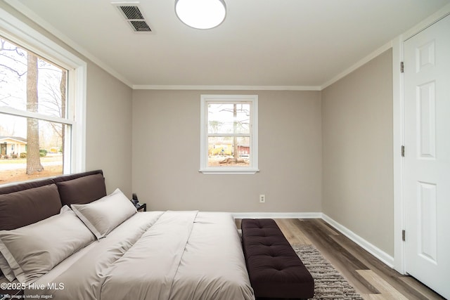 bedroom with baseboards, wood finished floors, visible vents, and ornamental molding