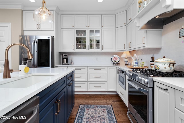 kitchen with blue cabinets, stainless steel appliances, custom range hood, light countertops, and white cabinetry