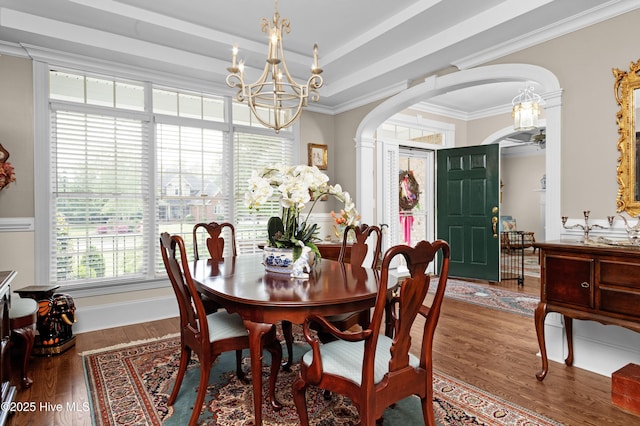 dining room featuring crown molding, arched walkways, a notable chandelier, and wood finished floors