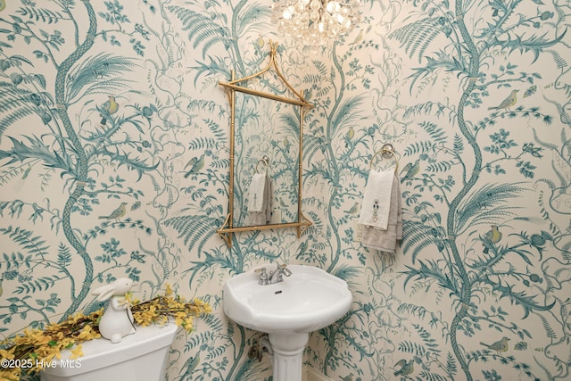 half bath featuring toilet, wallpapered walls, and a chandelier