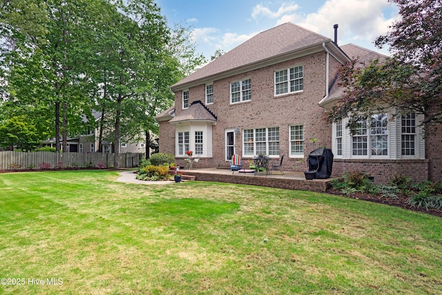 rear view of property featuring a lawn, brick siding, fence, and a patio area