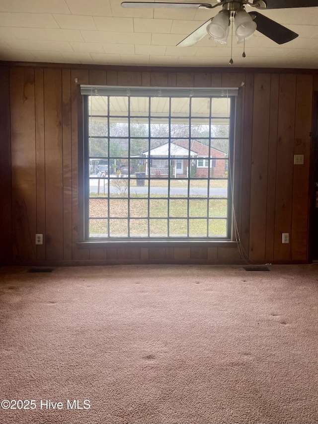 carpeted empty room featuring a ceiling fan and wood walls