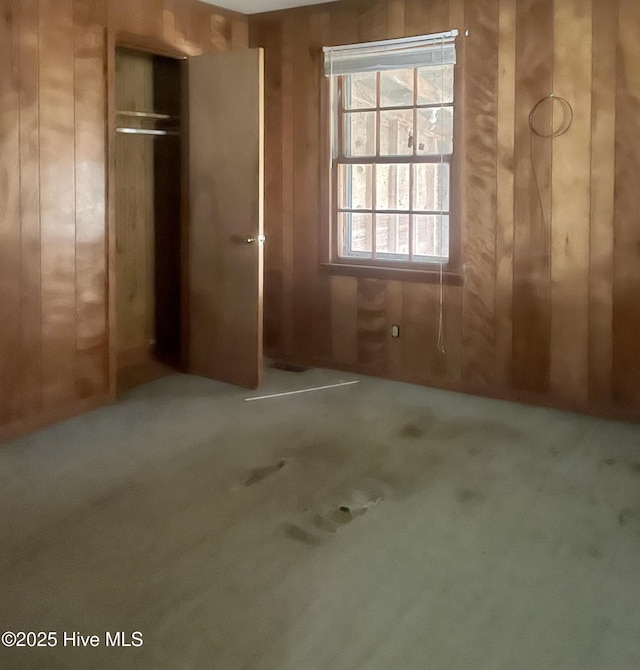 unfurnished bedroom featuring wood walls, carpet flooring, and a closet
