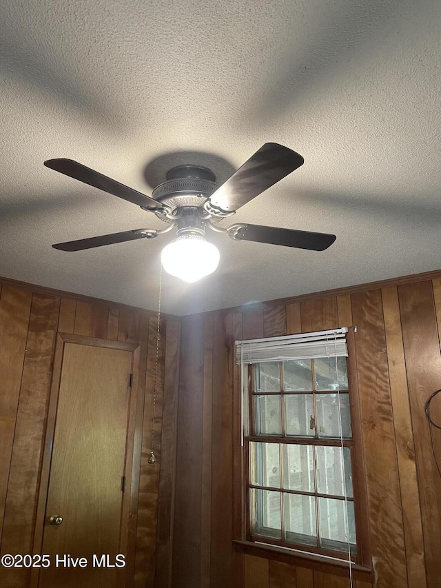 interior details featuring a ceiling fan, wood walls, and a textured ceiling