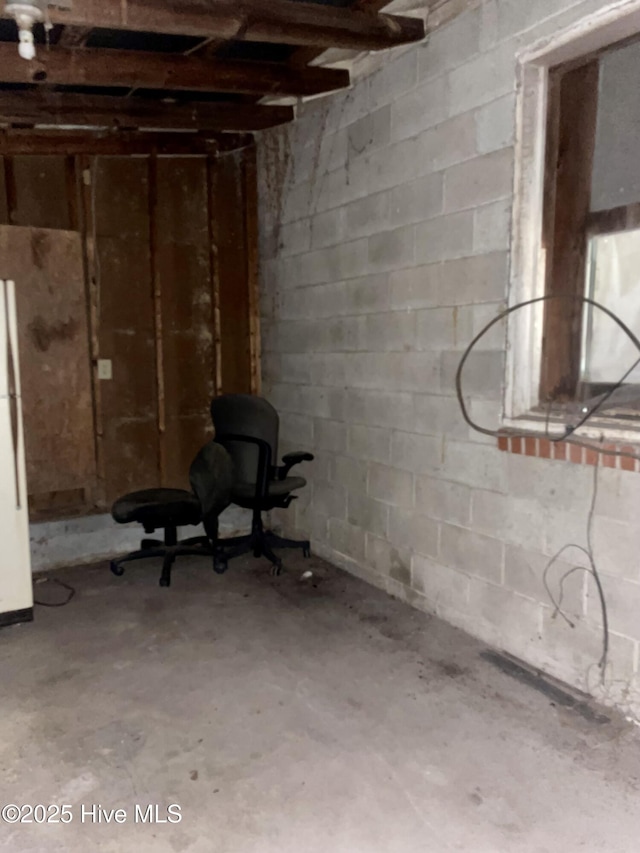 unfinished basement with concrete block wall and freestanding refrigerator
