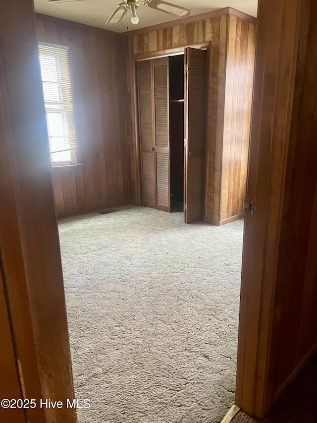 unfurnished bedroom featuring wooden walls, ceiling fan, carpet floors, and a closet