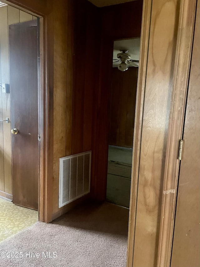 hallway featuring visible vents, wood walls, and carpet floors