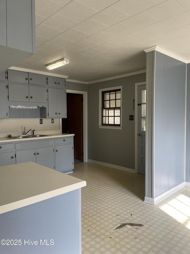 kitchen featuring a sink, crown molding, baseboards, light countertops, and light floors