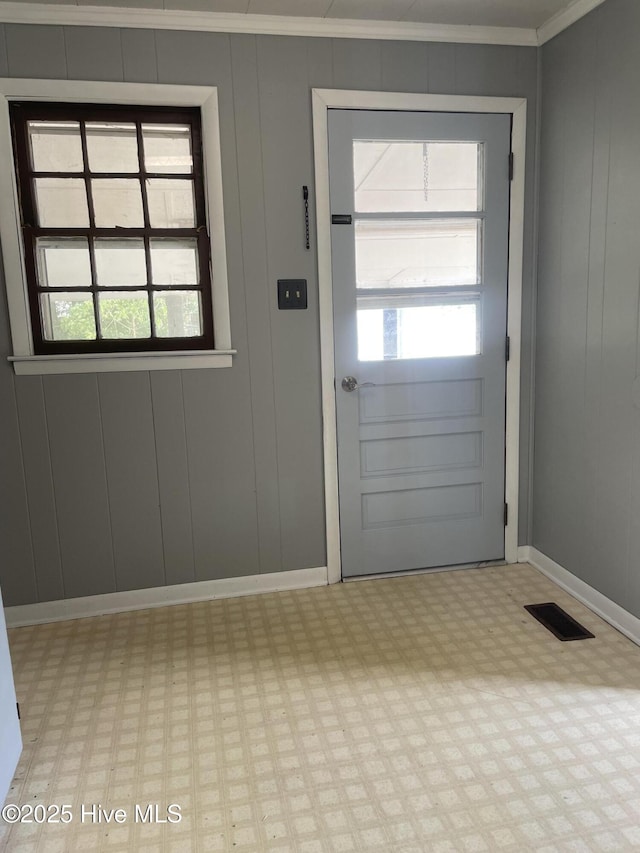 doorway to outside featuring crown molding, visible vents, a decorative wall, baseboards, and light floors