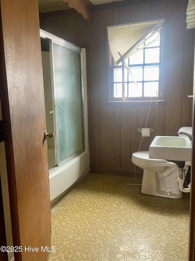bathroom with combined bath / shower with glass door, toilet, baseboards, and a sink