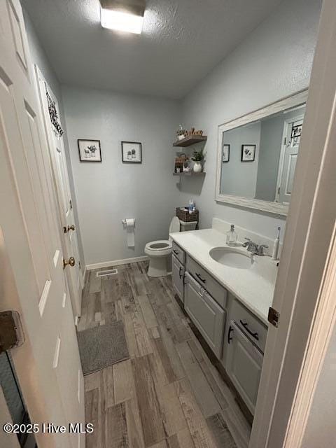 bathroom with toilet, a textured ceiling, wood finished floors, baseboards, and vanity