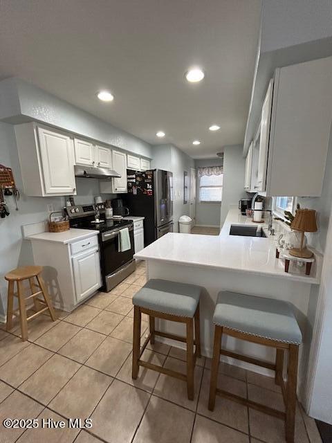 kitchen featuring a sink, under cabinet range hood, a peninsula, appliances with stainless steel finishes, and a breakfast bar area