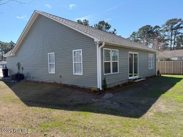 view of side of home with central air condition unit, a yard, and fence