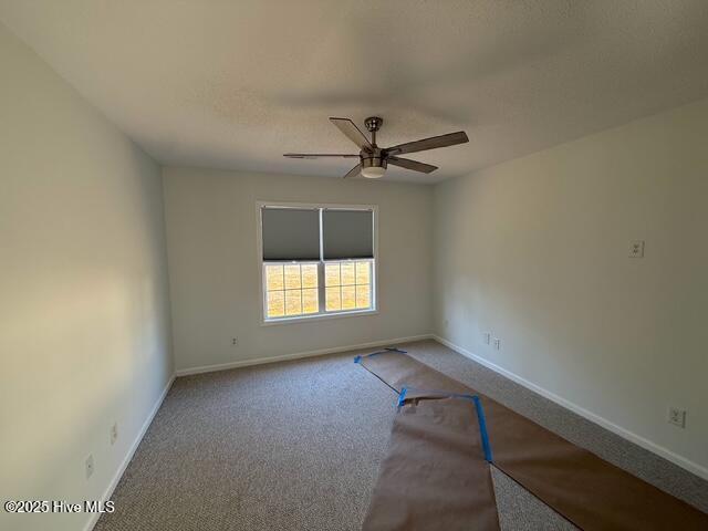 carpeted spare room featuring baseboards and ceiling fan