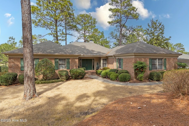 ranch-style house featuring brick siding, a chimney, and roof with shingles