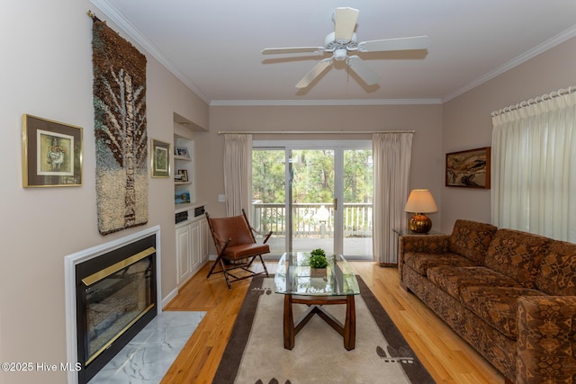 living room featuring a tiled fireplace, light wood-style flooring, a ceiling fan, and ornamental molding