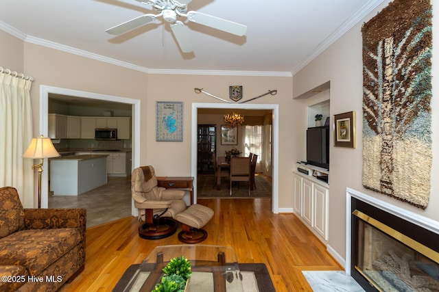 living area featuring a fireplace with flush hearth, ceiling fan with notable chandelier, light wood-style floors, and ornamental molding