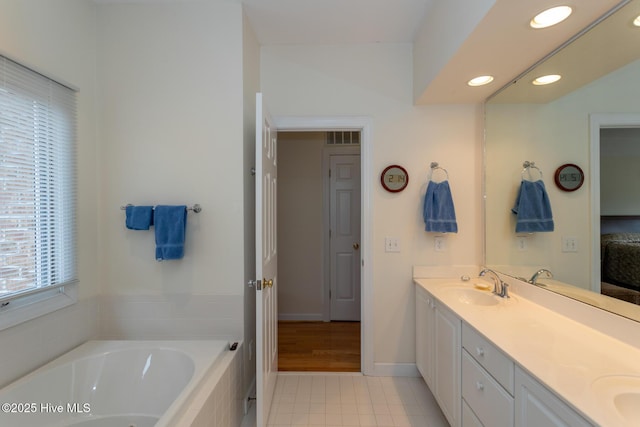 ensuite bathroom featuring tile patterned flooring, double vanity, recessed lighting, a bath, and a sink