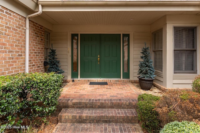 view of exterior entry with a porch and brick siding