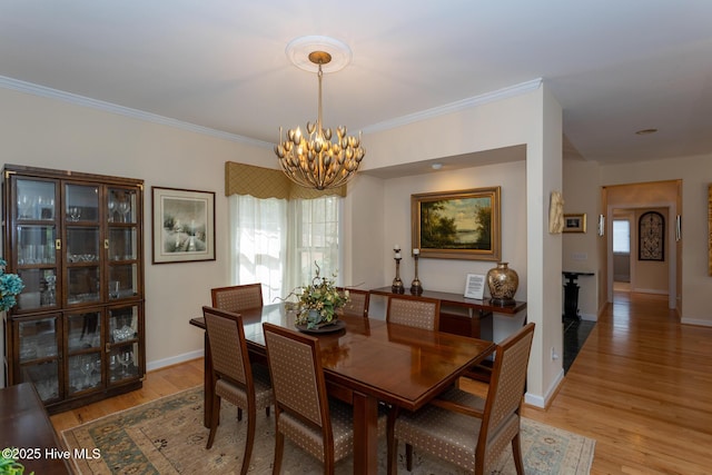 dining space with light wood finished floors, a wealth of natural light, an inviting chandelier, and ornamental molding