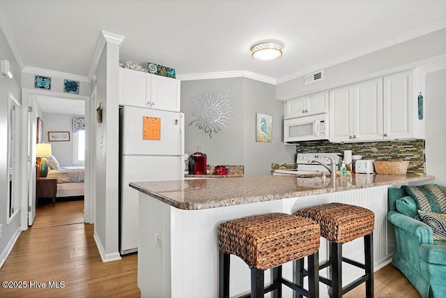 kitchen with visible vents, a peninsula, light wood-style floors, white appliances, and a sink