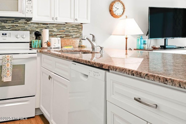 kitchen with white appliances, light stone countertops, a sink, white cabinets, and backsplash